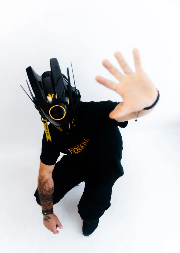 L'Empereur vêtu d'un casque cyberpunk et d'un t-shirt en exclusivité lève la main vers l'objectif comme pour faire signe qu'il veut avoir recours à la politique de retours et de remboursements