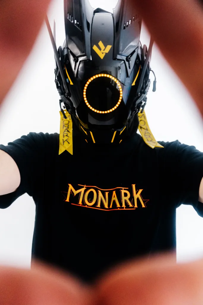 L'Empereur cyberpunk portant un masque robotique et arborant un des t-shirts Monark streetwear royal en formant un triangle avec ses mains devant l'objectif